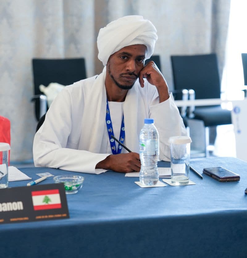 A delegate in white Sudanese dress listening during a summit session.