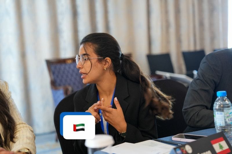 A delegate speaking during a session with a United Arab Emirates flag on the table.